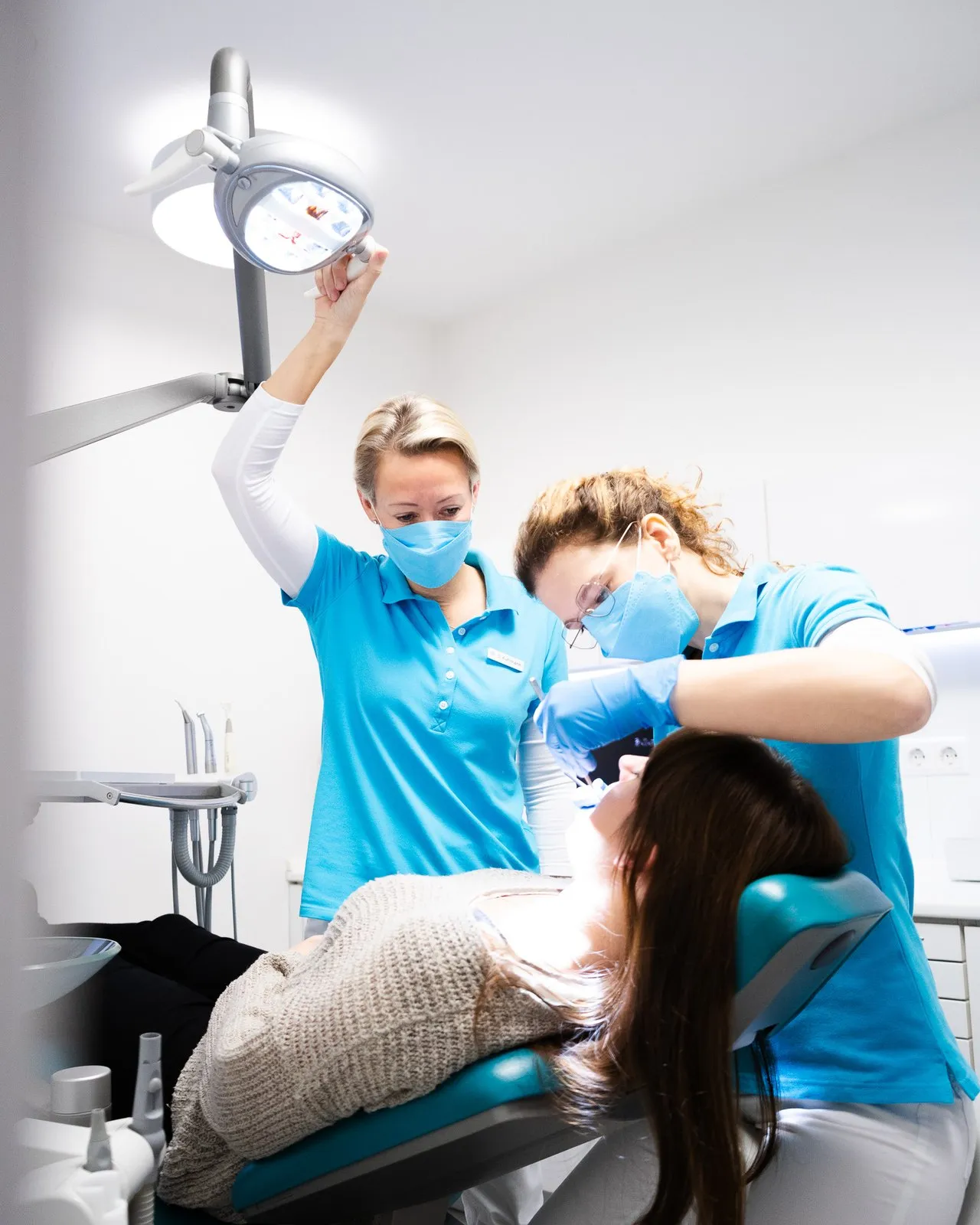 Zahnärztin und Assistenz behandeln Patientin im Behandlungsstuhl in Praxis.