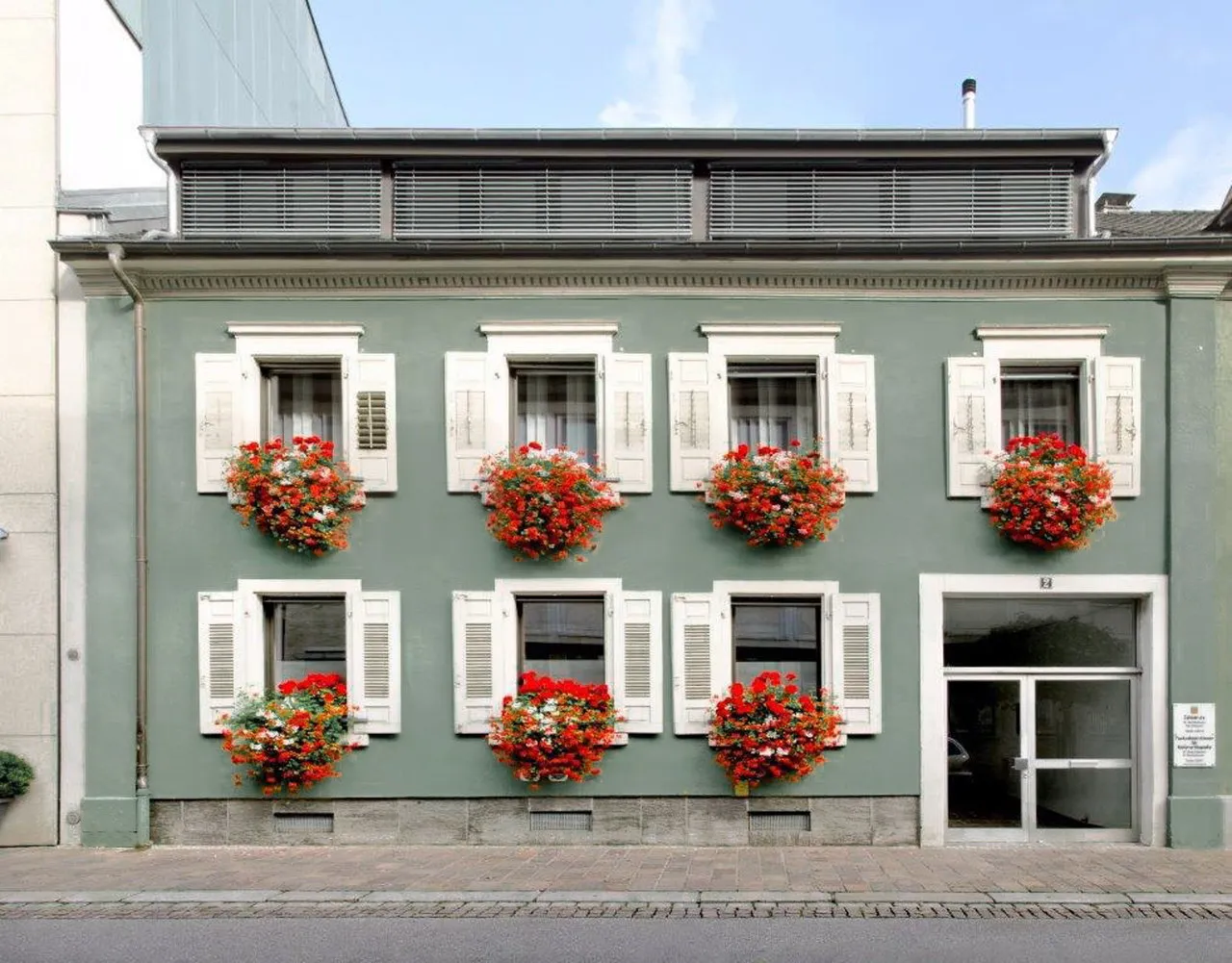Hausfassade mit weißen Fensterläden und roten Geranien-Blumenkästen